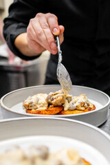 A chef's hand carefully drizzles creamy sauce over two beautifully plated pancakes topped with mushrooms and savory ingredients, showcasing culinary artistry in a professional kitchen.