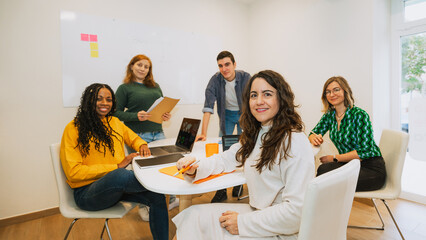 A diverse group of young professionals poses for the camera during a business meeting in a coworking space. Collaborative and friendly work environment