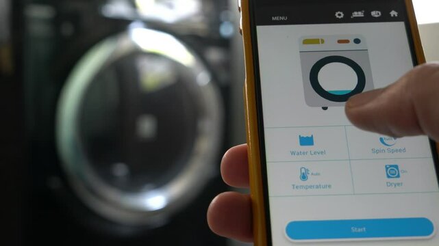 A person is holding a cell phone that is displaying a laundry room. The phone is showing a bed and a washing machine