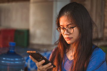 Young woman with glasses focused on her smartphone in warm sunlight.