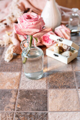 A rose in a glass vase and sentimental keepsakes around it.