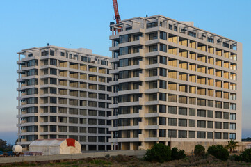 Fototapeta premium Modern apartment buildings under construction at dusk near the coastline with a clear sky and distant crane