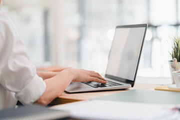 Person working on white screen laptop at desk in bright office environment, with plant and documents nearby, creating productive and focused atmosphere