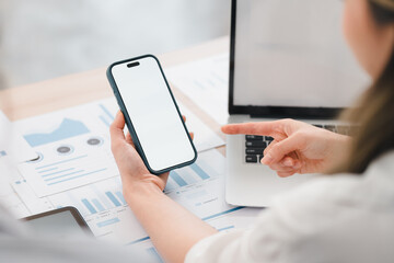 Person holding smartphone with blank screen while discussing data charts and graphs on desk, indicating business or analytical context