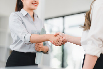 Fototapeta premium professional handshake between two women in modern office setting, symbolizing agreement, partnership, or collaboration. bright and open environment enhances positive and professional mood