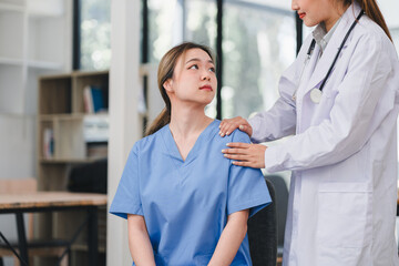 female doctor in white coat offers support to nurse in blue scrubs, placing hand on her shoulder in...