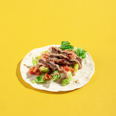 sliced beef and vegetable with spicy sauce on a flour tortilla wrap, on a yellow vibrant background