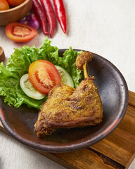 indonesian traditional ayam greprek, a fried chicken with sambal chili sauce on top of it, on a white wooden background.