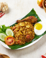 Indonesian fried rice with fried chicken and sunny side up egg on a banana leaves in white wooden background.
