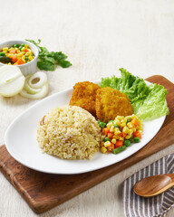Fried chicken katsu with butter rice and vegetable, in a white plate on a wooden background
