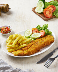 Fried fish and chips with vegetable pickles, in a white plate on a white wooden background
