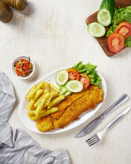 Fried fish and chips with vegetable pickles, in a white plate on a white wooden background
