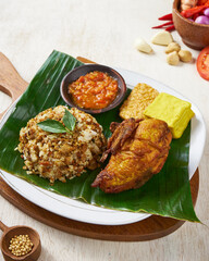 Indonesian fried chicken with spiced rice, tempe and tofu, on top of banana leaves, in a wooden background