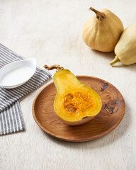 delicious sliced honey pumpkin with coconut cream sauce on a wooden plate in a white wooden background.