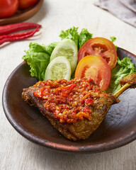 indonesian traditional ayam greprek, a fried chicken with sambal chili sauce on top of it, on a white wooden background.