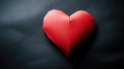 A lone red paper heart on a dark black background, perfect for romantic occasions or as a symbol of love and passion