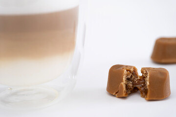 A caramel candy with a soft filling paired with a latte in Mocha Mousse color, set against a white surface. A stylish concept for cafes, restaurants, and food blogs.