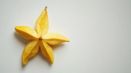 A bright yellow fruit resembling a flower rests on a clean white surface, showcasing its unique shape and vibrant color.
