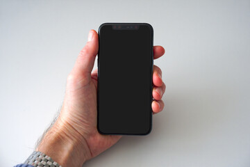 Close-up of male hand holding smartphone with blank black screen against white background. Photo taken January 19th, 2025, Zurich, Switzerland.