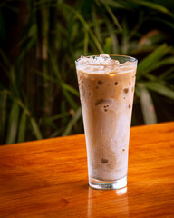 Iced coffee latte on the brown wooden table. Isolated from dark leaf background. Perfect for menu, catalogue, advertising or commercial use