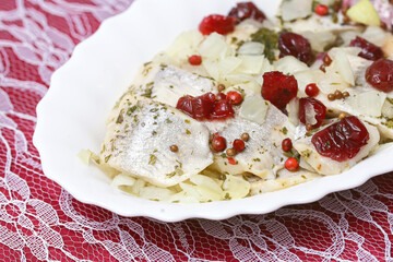 Marinated herring with cranberries and pepper served on a white plate. Sweet and spicy flavour. Herrings sprinkle with spices. Pickled fish background.