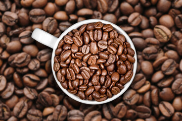 Cup filled with coffee beans. Dark coffee seeds on a textured background. Fresh morning caffeine aroma. Americano mug in a cafe setting. Brown beverage concept.