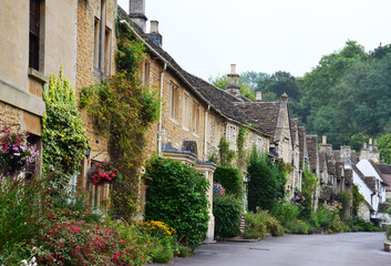 Fototapeta premium Traditional stone houses on a road decorated with plants in picturesque Castle Combe village, Cotswolds, Wiltshire, UK