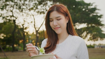 Portrait Asian woman eating healthy fresh salad, Beautiful young woman with Healthy Food. Vegan Salad. Diet. Dieting Concept. Healthy Lifestyle. Fit woman eating salad after working out in sunny park