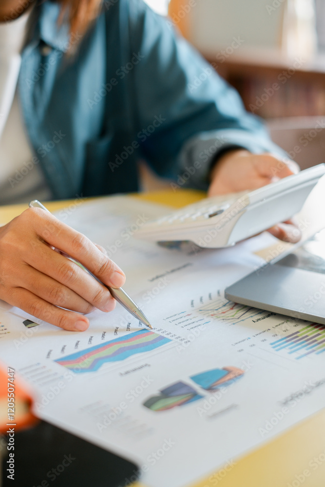 Poster close-up of a person using a calculator and reviewing financial charts and graphs on paper in an off