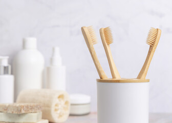 Eco-friendly wooden toothbrushes in holder cup in a white in bathroom against natural cosmetics, mockup