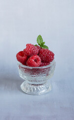 Fresh raspberries and mint leaves resting in glass bowl