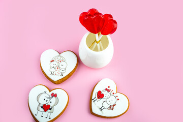 Gingerbread cookies and red heart-shaped lollipops for Valentine's Day on a pink background, sweet Valentine's Day gift, cookies with cream and icing, banner