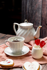 tea in a white porcelain cup and saucer, next to gingerbread cookies with white glaze, red heart-shaped lollipops, Valentine's Day composition, Valentine's Day tea party, bouquet of multi-colored gyps