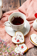 tea in a white porcelain cup and saucer, next to gingerbread cookies with white glaze, red heart-shaped lollipops, Valentine's Day composition, Valentine's Day tea party, bouquet of multi-colored gyps