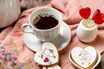 tea in a white porcelain cup and saucer, next to gingerbread cookies with white glaze, red heart-shaped lollipops, Valentine's Day composition, Valentine's Day tea party, bouquet of multi-colored gyps