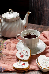 tea in a white porcelain cup and saucer, next to gingerbread cookies with white glaze, red heart-shaped lollipops, Valentine's Day composition, Valentine's Day tea party, bouquet of multi-colored gyps