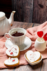 tea in a white porcelain cup and saucer, next to gingerbread cookies with white glaze, red heart-shaped lollipops, Valentine's Day composition, Valentine's Day tea party, bouquet of multi-colored gyps
