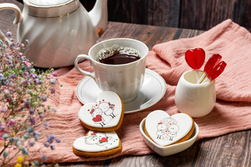 tea in a white porcelain cup and saucer, next to gingerbread cookies with white glaze, red heart-shaped lollipops, Valentine's Day composition, Valentine's Day tea party, bouquet of multi-colored gyps