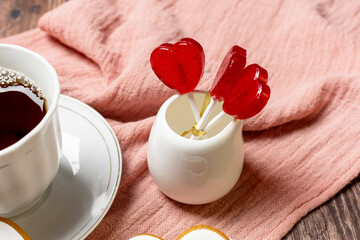 tea in a white porcelain cup and saucer, red heart-shaped lollipops in a white vase, Valentine's Day composition, Valentine's Day tea party, bouquet of colorful gypsophila, wooden background