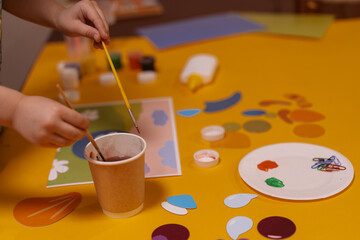 Child paints and makes a collage of colored paper