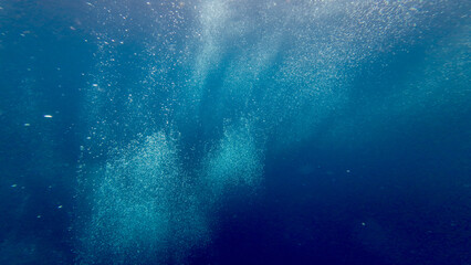 Air bubbles underwater. Air bubbles rise from the depths of the ocean to the surface through the thickness of the water. Air bubbles against the background of the blue abyss of the sea.