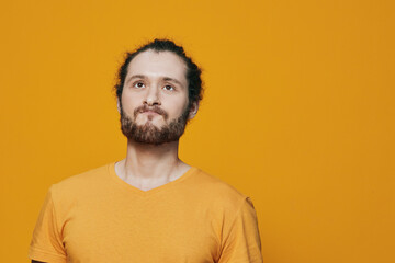 Fototapeta premium Male model with beard and bun hairstyle smiling against a bright yellow background, wearing a casual orange T shirt, evoking a positive and cheerful mood