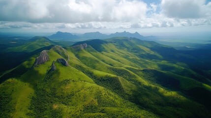 Obraz premium Aerial view of rolling green hills with rocky outcroppings under a cloudy sky