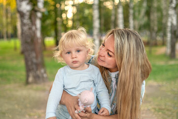 A happy mother plays with her son outside in the park on a sunny summer day. Mom and baby have fun together. The concept of family, happiness and love.