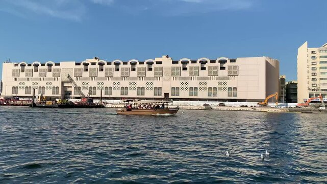 Traditional boat sails through Dubai creek. Motion of water. Deira Old Souk ferry station in the background. View from a boat. Dubai, United Arab Emirates 