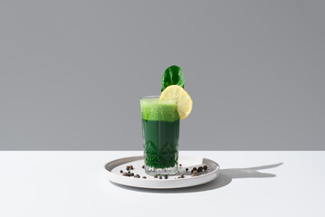 Jugo batido de espinacas adornado con una rodaja de limón sobre una mesa blanca y fondo gris