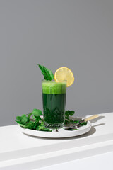 Jugo batido de espinacas adornado con una rodaja de limón sobre una mesa blanca y fondo gris