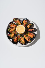 Plato de mejillones al vapor rellenos con vinagreta de tomate, pimiento rojo, pimiento verde, cebolla y limón sobre fondo blanco