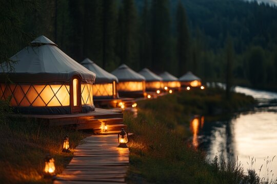 A line of yurts stretching along a riverbank, with reflections shimmering in the water and trees swaying in the breeze