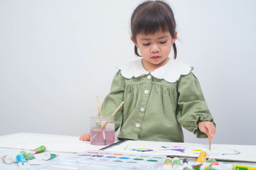 A young girl engages in creative painting activities at a bright table, showcasing her artistic...